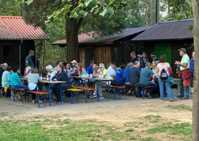 Hütte im Freien, davor Tische und Bänke und Wanderer
